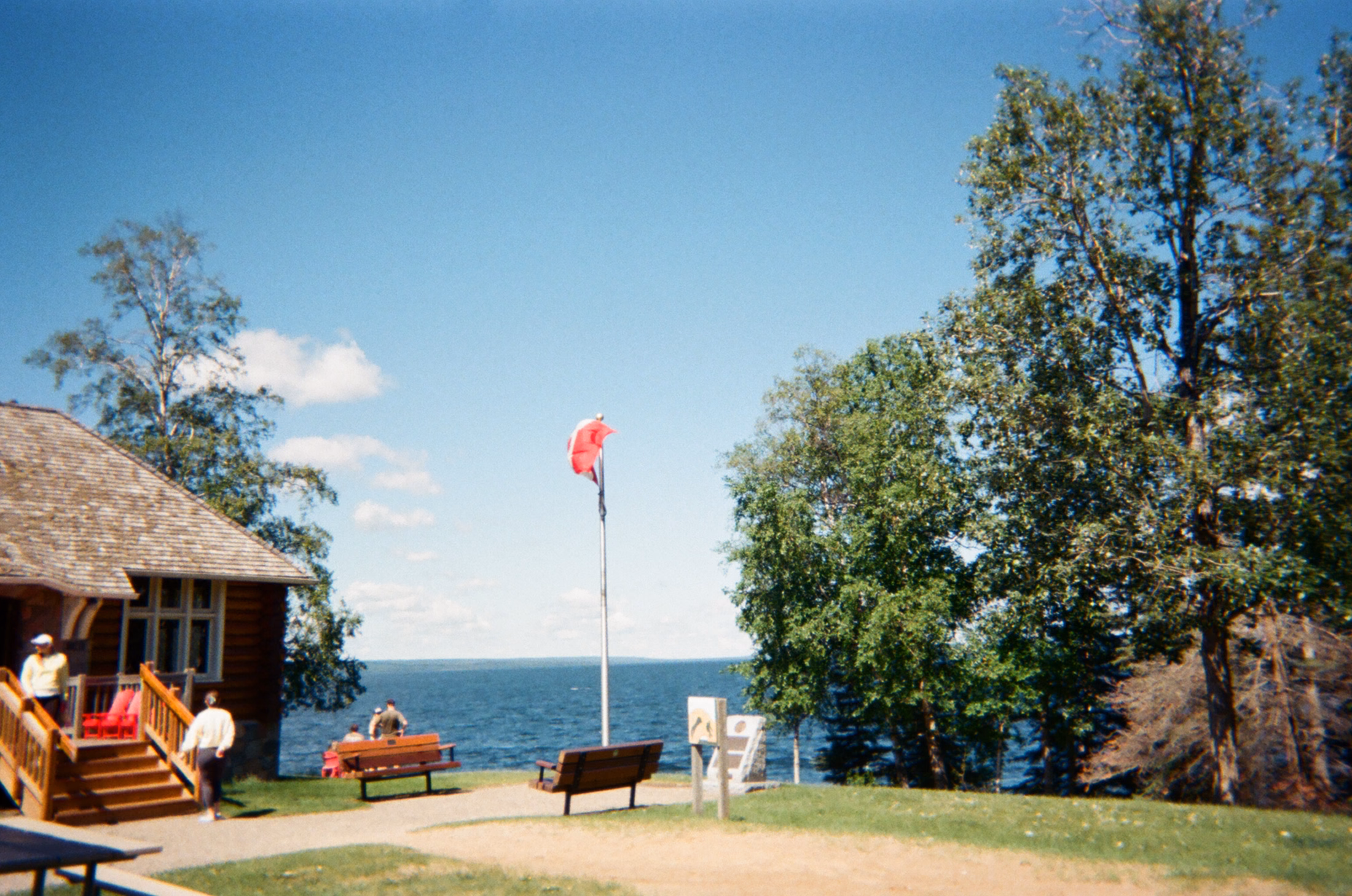 Vintage film photograph of a lakeside cabin beneath a bright blue sky